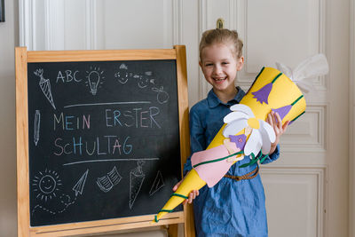 Cheerful girl standing by blackboard at home