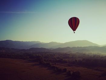 Hot air balloon flying over mountains against clear sky