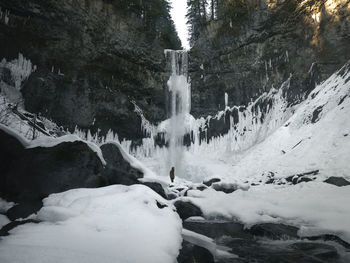 Man standing on snow covered land against waterfall