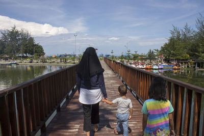 Rear view of people on footbridge against sky