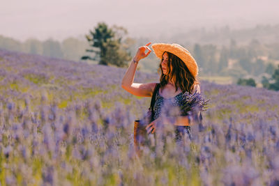 Portrait of woman in a straw hat standing in lavender flowers field, looking in the distance