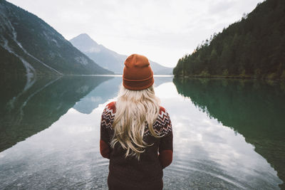 Rear view of woman standing by lake against mountain