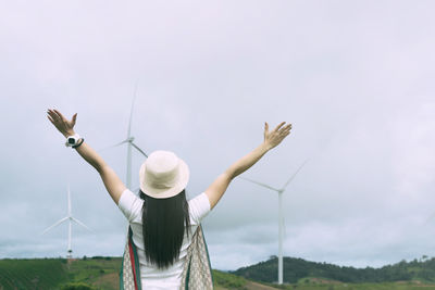 Rear view of woman with arms outstretched against sky