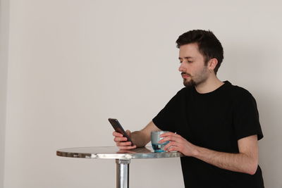 Young man using mobile phone against wall