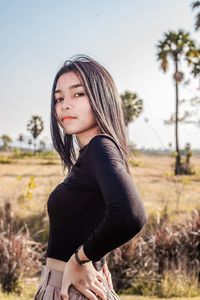 Side view of young woman standing on field against sky