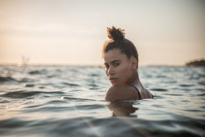 Portrait of young woman swimming in sea against sky