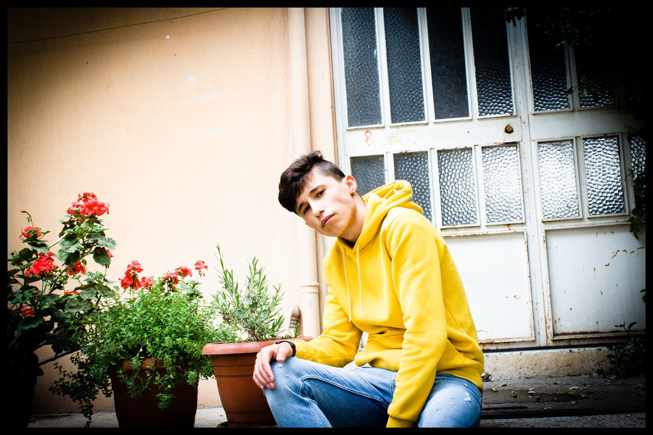 real people, yellow, one person, sitting, leisure activity, young men, young adult, lifestyles, architecture, casual clothing, day, side view, built structure, three quarter length, looking, window, outdoors, building exterior, plant, contemplation