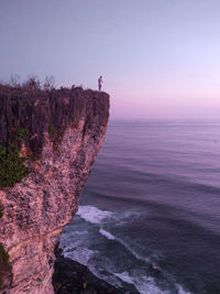 Man standing on rock by sea against sky during sunset