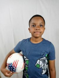 Portrait of boy with ball standing against white background