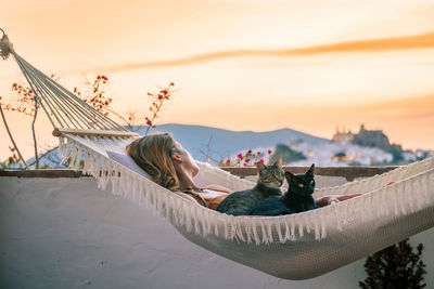 Rear view of woman sitting on beach against sky during sunset