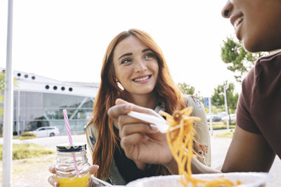 Smiling redhead woman holding mason jar looking at female friend