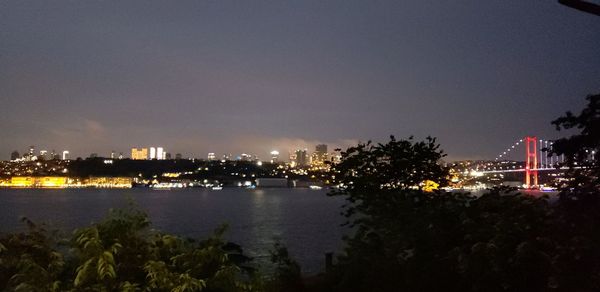 Illuminated buildings by river against sky at night