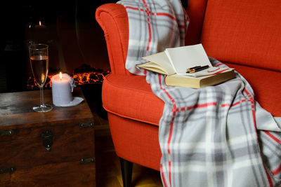 Soft blanket, book, notepad and pen on elegant armchair, a glass of wine and candle beside it.