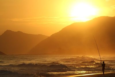 Silhouette of man fishing at sea shore during sunset