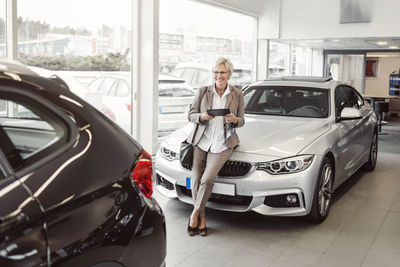 Happy businesswoman with digital tablet looking at car in store