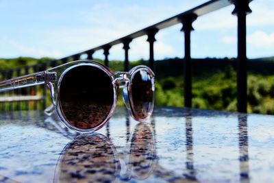 Close-up of sunglasses on glass against lake