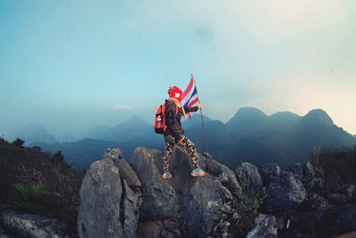 Full length of woman with thai flag standing on rocks against sky