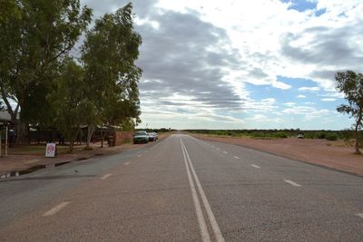 Empty road along trees and against sky