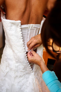 Close-up of a mother button up the white wedding dress of her daughter