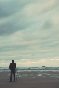 Man photographing at beach against sky during sunset