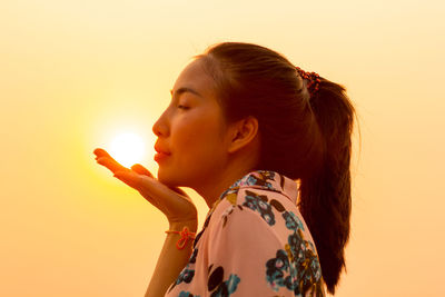 Optical illusion of young woman blowing sun against clear orange sky