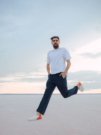 Portrait of young man running on sand at beach against sky