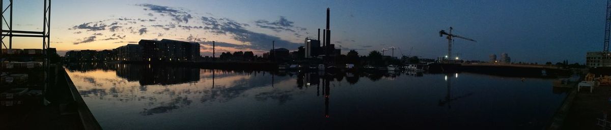 Scenic view of lake by silhouette buildings against sky at sunset