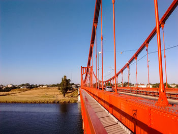 Suspension bridge over river against clear blue sky