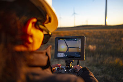 Female drone pilot flies in a wind farm at sunrise