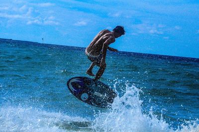 Man surfing in sea against blue sky