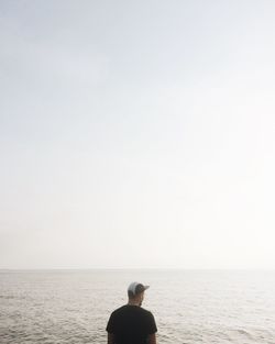 Rear view of man standing by sea against clear sky on sunny day