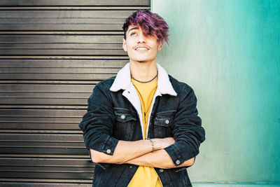 Fashionable teenage boy standing with arms crossed against wall