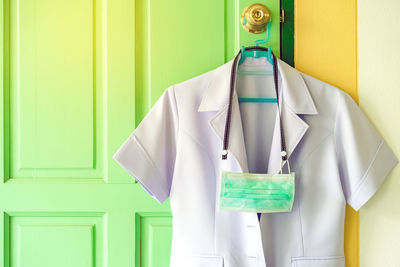 Close-up of laboratory coat hanging with mask by door