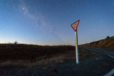 Road sign on field against clear sky at night