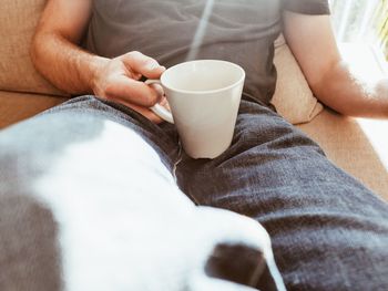 Midsection of man holding hot coffee cup while resting on sofa