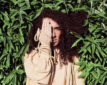 Portrait of woman covering face with hand against plants