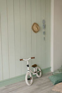 Children's white bicycle for small children stands near a light wooden wall in the house