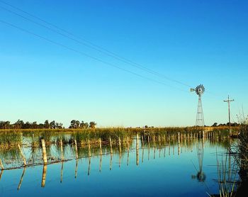 Electricity pylon by lake against clear sky