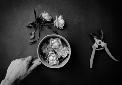 Cropped hand of person holding flowers in container on table