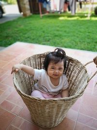 Portrait of cute baby girl sitting in basket at yard