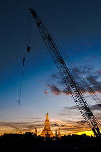 Low angle view of cranes at construction site against sky during sunset