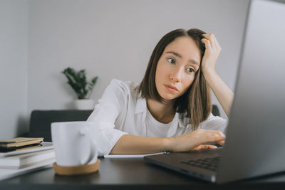 Portrait of young woman using mobile phone while sitting on table.