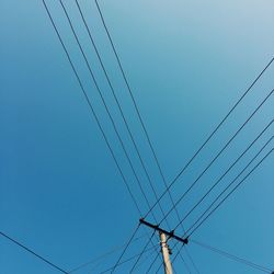 Low angle view of electricity pylon against clear blue sky