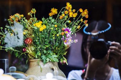 Reflection of woman photographing flower vase on glass