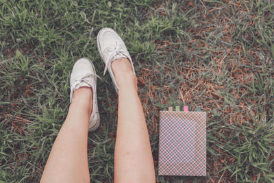 Low section of woman sitting by book on grass