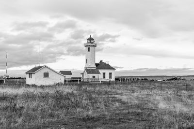 Lighthouse on field by building against sky