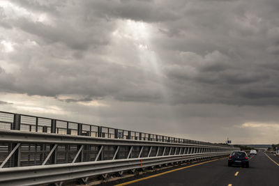 Cars on road in city against storm clouds