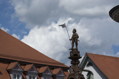 Low angle view of statue in residential district against cloudy sky