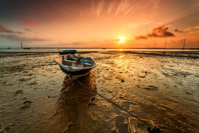 Boat moored on beach against sky during sunset