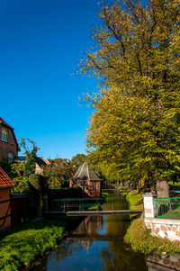 Canal amidst trees and buildings against blue sky